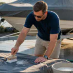 Boat owner cleaning a gray boat cover with mild soap near a covered trailered boat