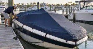 Boat owner fitting a navy mooring cover on a runabout in a marina wet slip